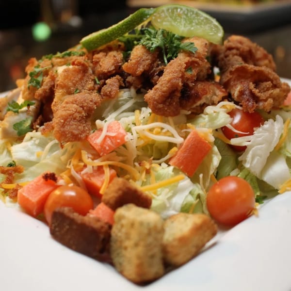 Crispy fried chicken salad with lettuce, tomatoes, cheese, croutons, and a lime wedge.