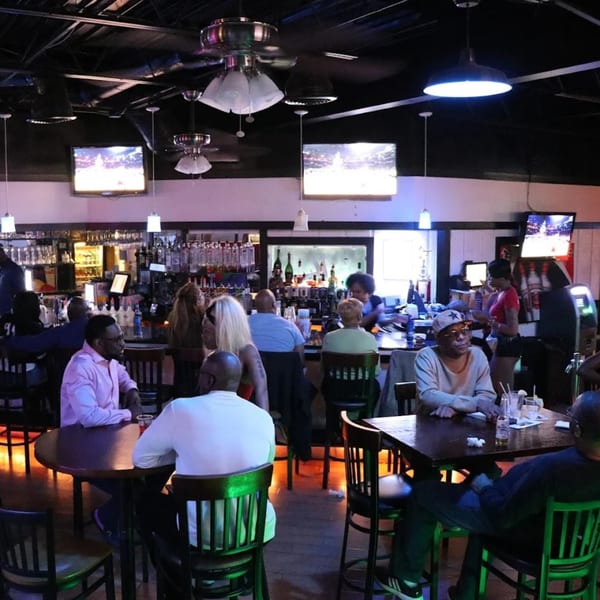Patrons socialize at tables and the bar inside Empire Lounge, with TVs and ceiling fans visible.