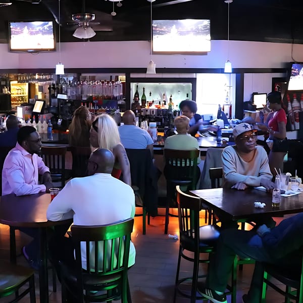 Patrons socialize at tables and the bar inside Empire Lounge, with TVs displaying content.