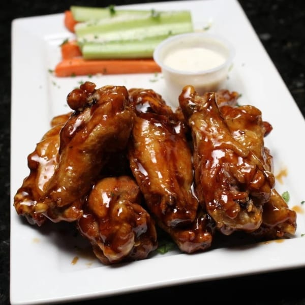 Empire Lounge's sticky glazed chicken wings with celery, carrots, and ranch dressing on a white plate.