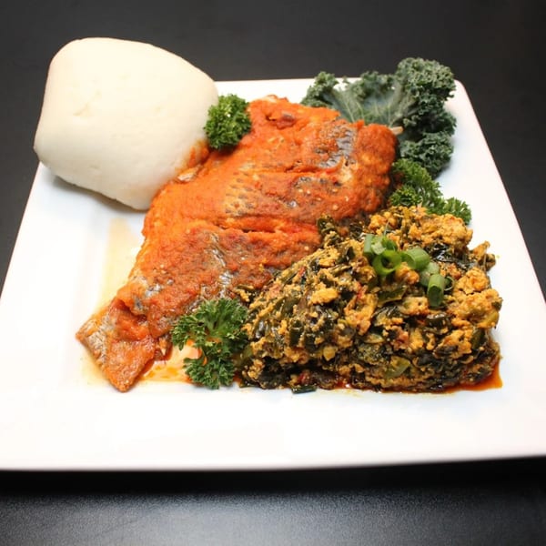 A plate of red snapper in tomato sauce, a side of green stew, and fufu.