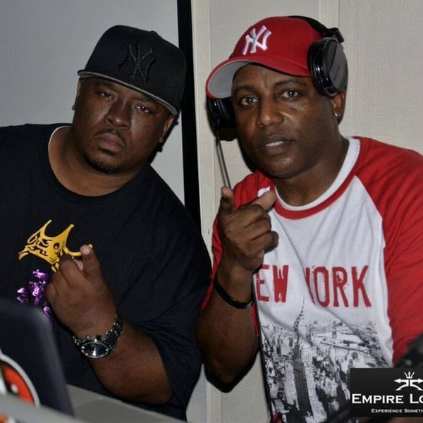 Two men in baseball caps, one with headphones, posing for a photo at Empire Lounge.