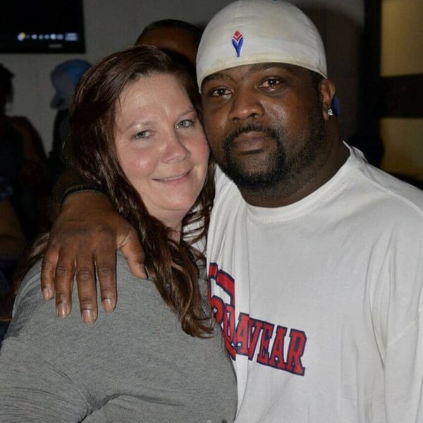 A smiling woman with long brown hair and a man in a white cap embracing at Empire Lounge.