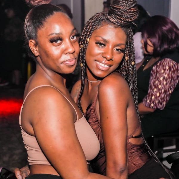 Two women smiling at the camera, one with a bun and the other with braids, at Empire Lounge.