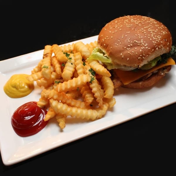 A burger with cheese, lettuce, and pickles, served with crinkle-cut fries, ketchup, and mustard.