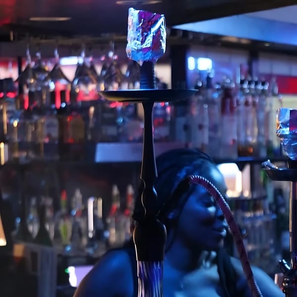 A hookah with foil-covered charcoal sits on a bar, with bottles and glasses in the background.