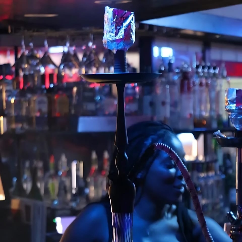 A hookah with foil-covered charcoal sits on a bar, with bottles and glasses in the background.