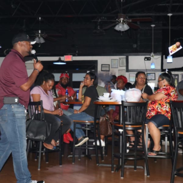 A man with a microphone addresses a group of people seated at high-top tables in Empire Lounge.