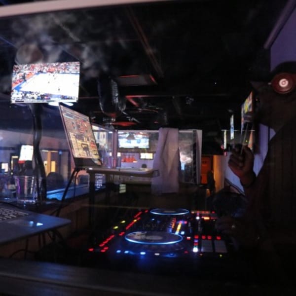 A DJ booth with glowing equipment, a laptop, and a person with headphones and a microphone.