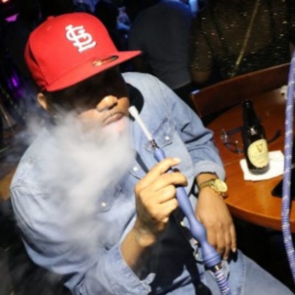 Man in a red cap and denim shirt exhaling smoke from a blue hookah at Empire Lounge.