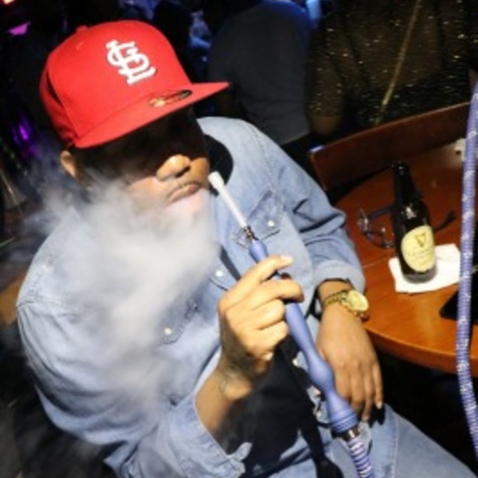 Man in a red cap and denim shirt exhaling smoke from a blue hookah at Empire Lounge.
