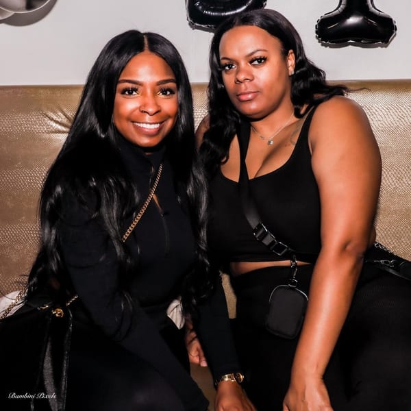 Two women in black outfits sitting on a gold textured bench at Empire Lounge.