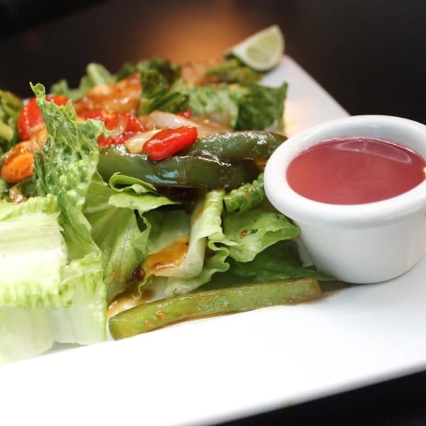 A fresh salad with green lettuce, red peppers, green beans, and a side of red dressing.