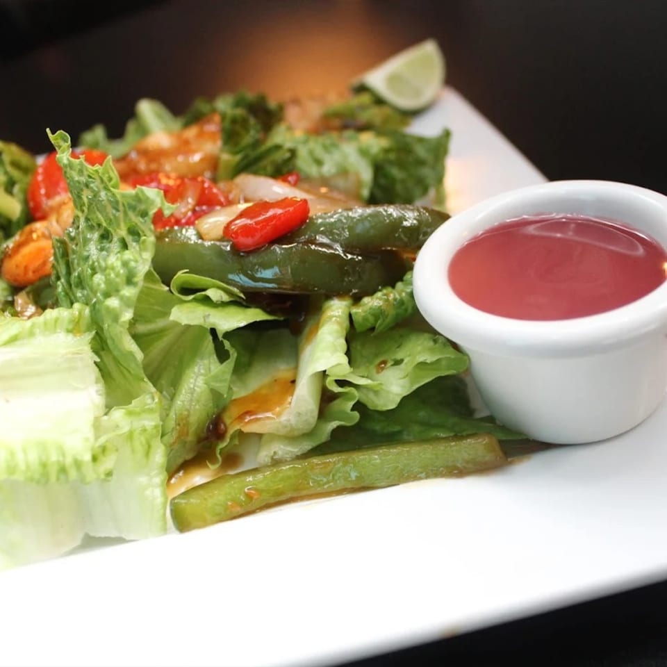 A fresh salad with green lettuce, red peppers, green beans, and a side of red dressing.