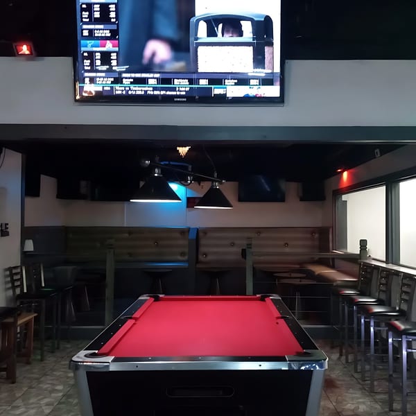A red-felt pool table in the Empire Lounge bar area with booths, bar stools, and a TV.