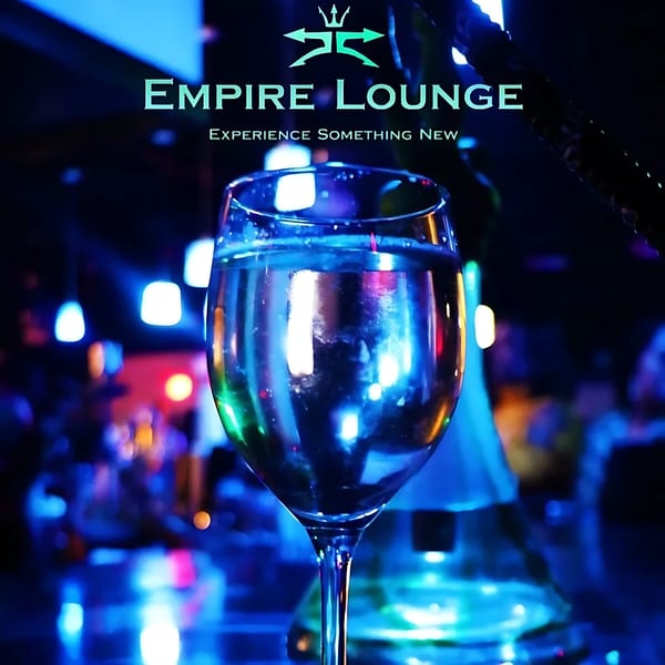 A wine glass with a drink, reflecting neon blue and pink lights, at Empire Lounge.