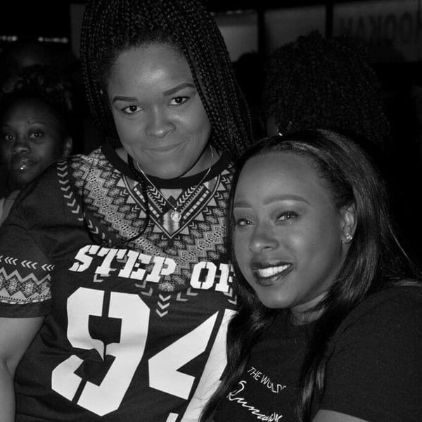 Two smiling women posing closely together in a dimly lit bar setting.
