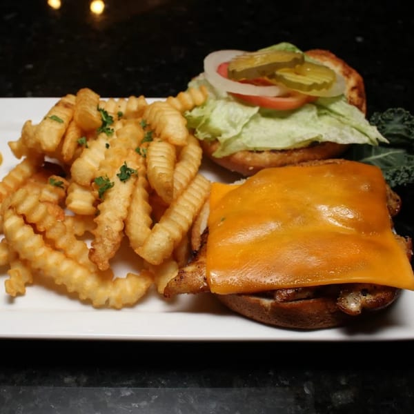 A grilled chicken sandwich with melted cheese, lettuce, tomato, onion, and pickles, served with crinkle-cut fries.